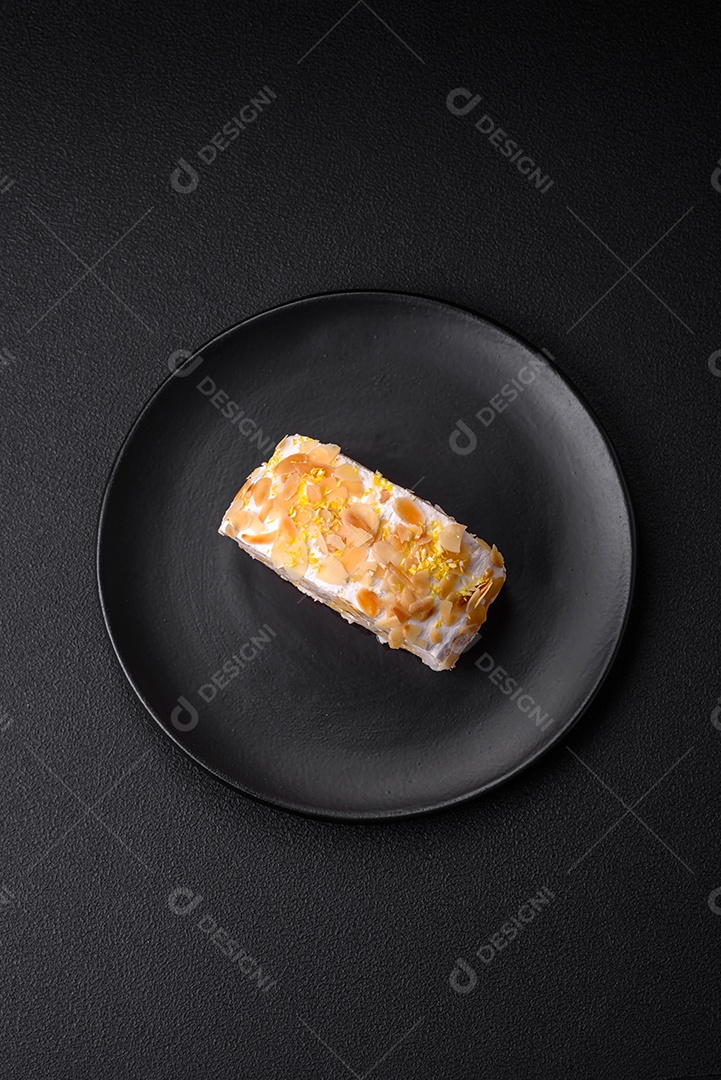 Rolo de merengue delicioso, fresco e doce com creme, lascas de amêndoa, nozes e frutas cortadas em fatias sobre um fundo escuro de concreto