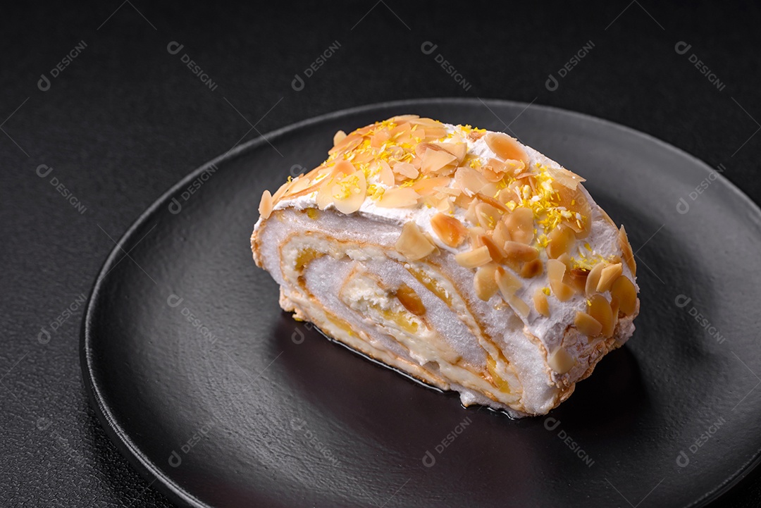 Rolo de merengue delicioso, fresco e doce com creme, lascas de amêndoa, nozes e frutas cortadas em fatias sobre um fundo escuro de concreto
