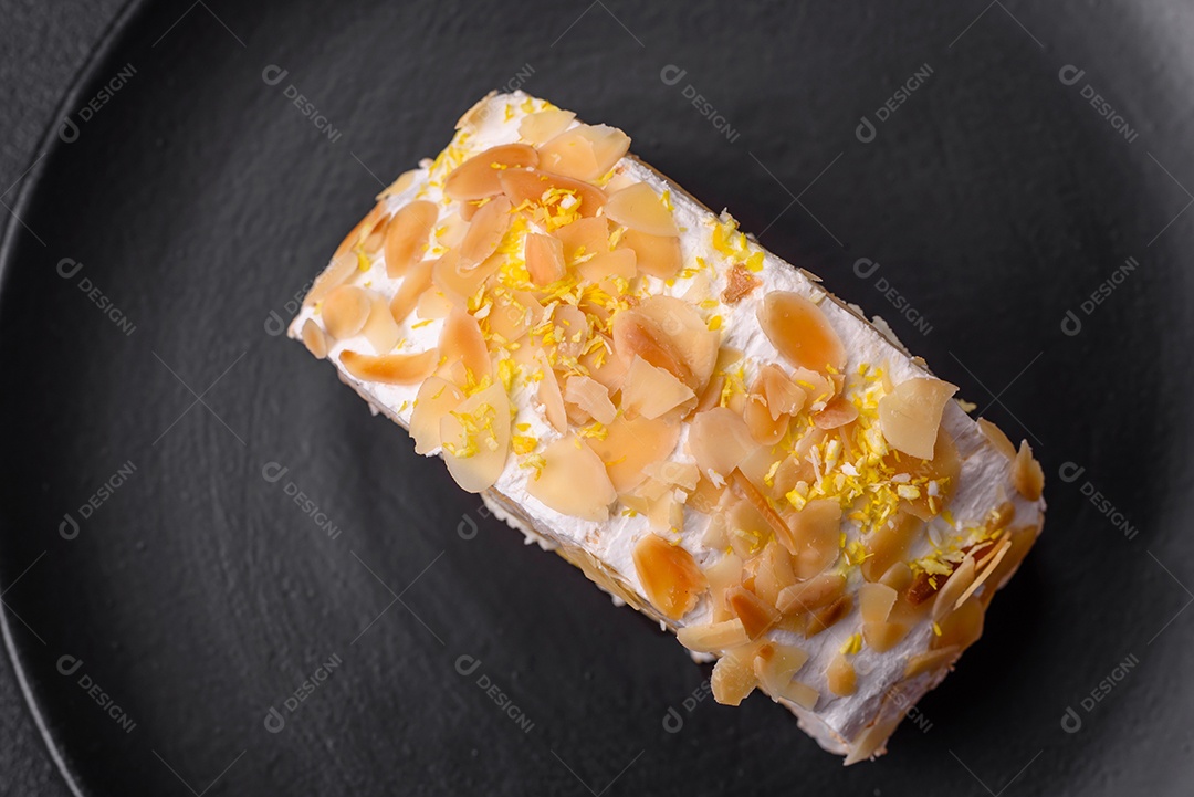 Rolo de merengue delicioso, fresco e doce com creme, lascas de amêndoa, nozes e frutas cortadas em fatias sobre um fundo escuro de concreto