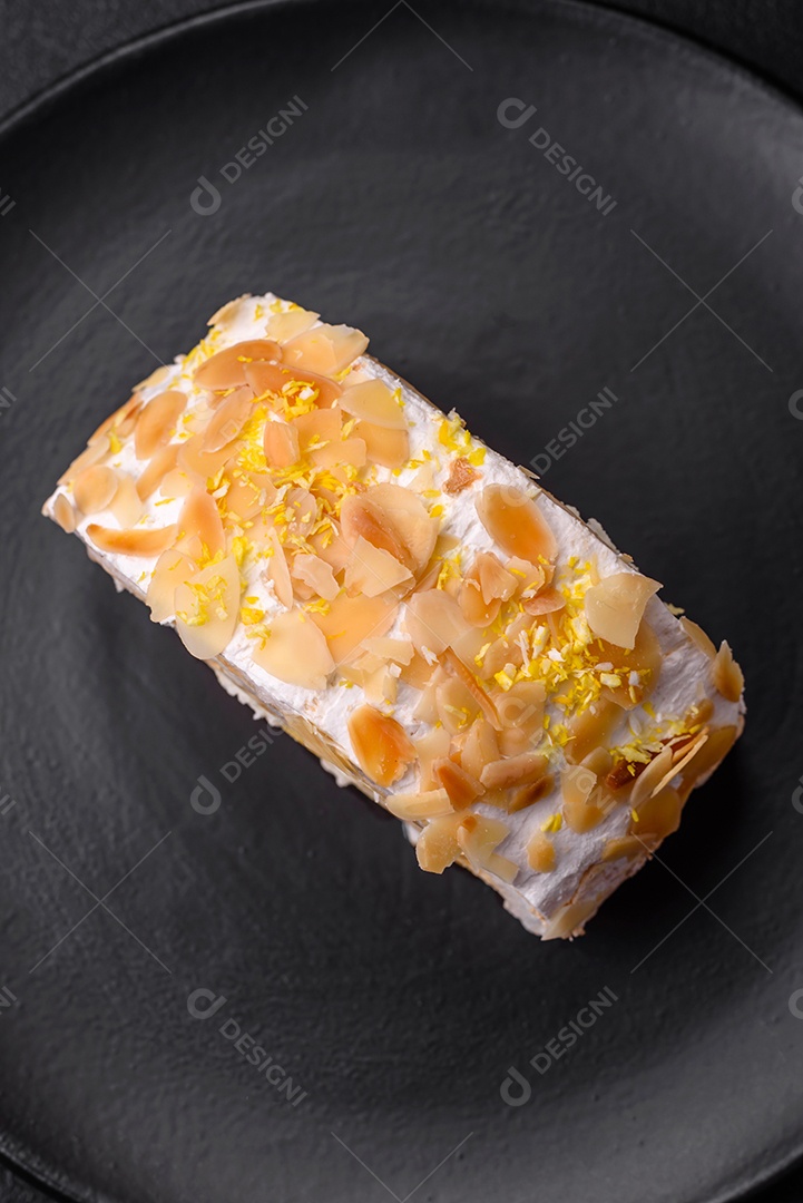 Rolo de merengue delicioso, fresco e doce com creme, lascas de amêndoa, nozes e frutas cortadas em fatias sobre um fundo escuro de concreto