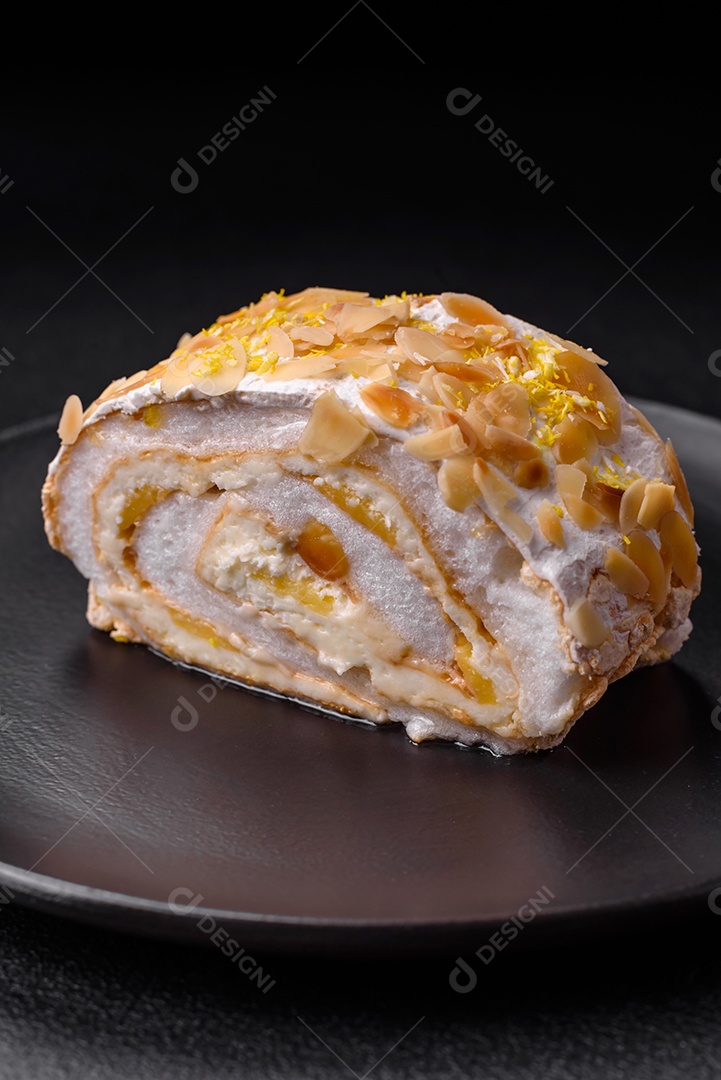 Rolo de merengue delicioso, fresco e doce com creme, lascas de amêndoa, nozes e frutas cortadas em fatias sobre um fundo escuro de concreto