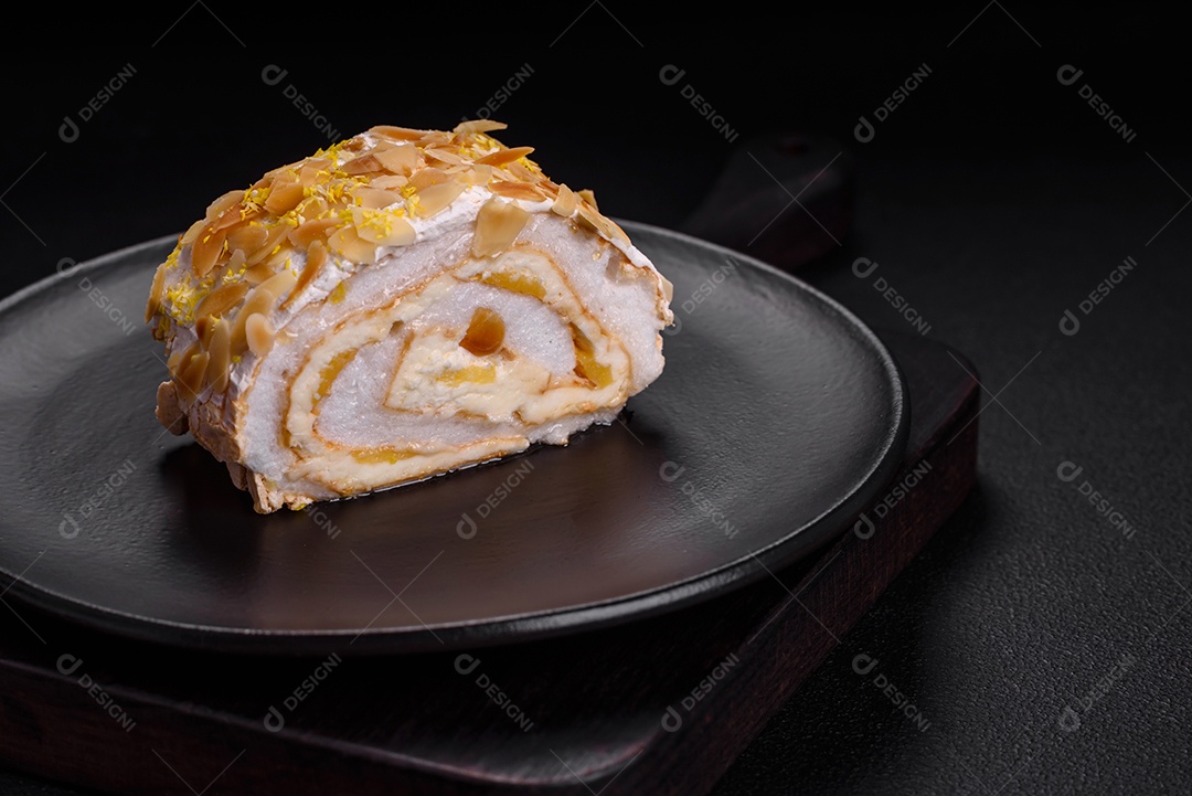 Rolo de merengue delicioso, fresco e doce com creme, lascas de amêndoa, nozes e frutas cortadas em fatias sobre um fundo escuro de concreto