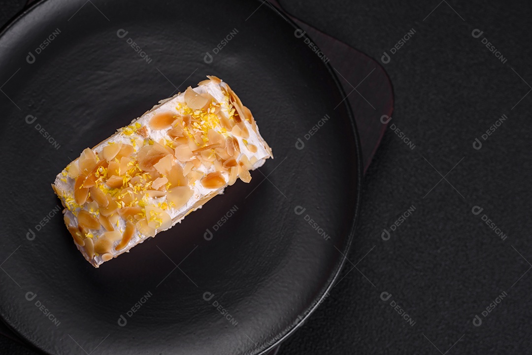 Rolo de merengue delicioso, fresco e doce com creme, lascas de amêndoa, nozes e frutas cortadas em fatias sobre um fundo escuro de concreto