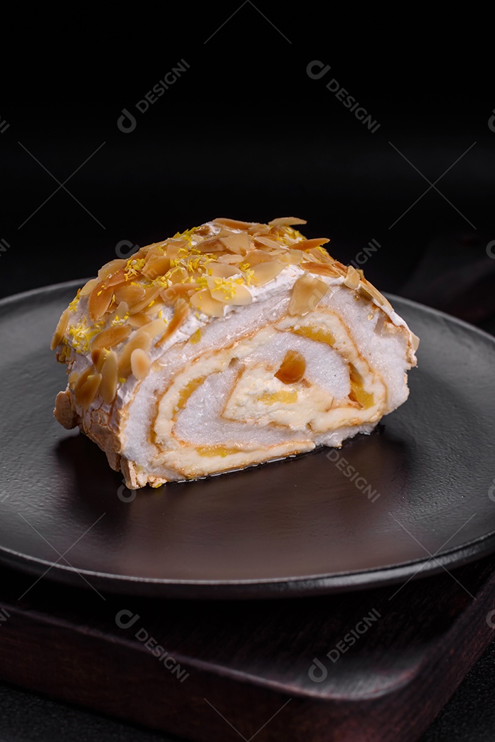 Rolo de merengue delicioso, fresco e doce com creme, lascas de amêndoa, nozes e frutas cortadas em fatias sobre um fundo escuro de concreto