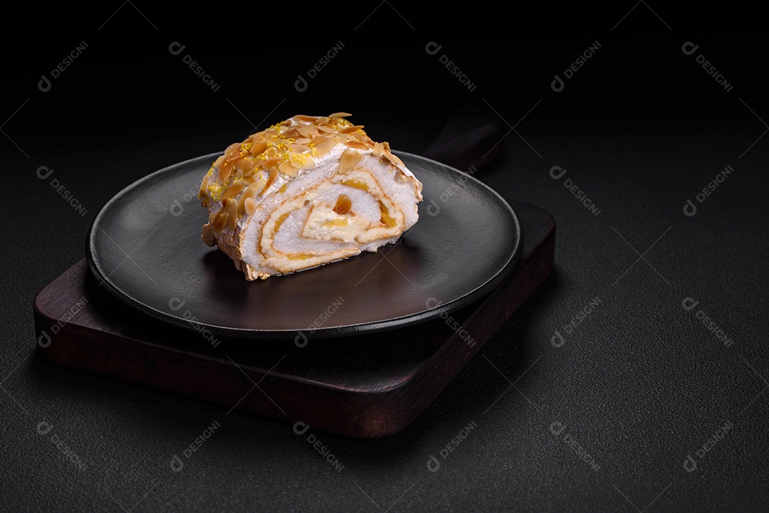 Rolo de merengue delicioso, fresco e doce com creme, lascas de amêndoa, nozes e frutas cortadas em fatias sobre um fundo escuro de concreto