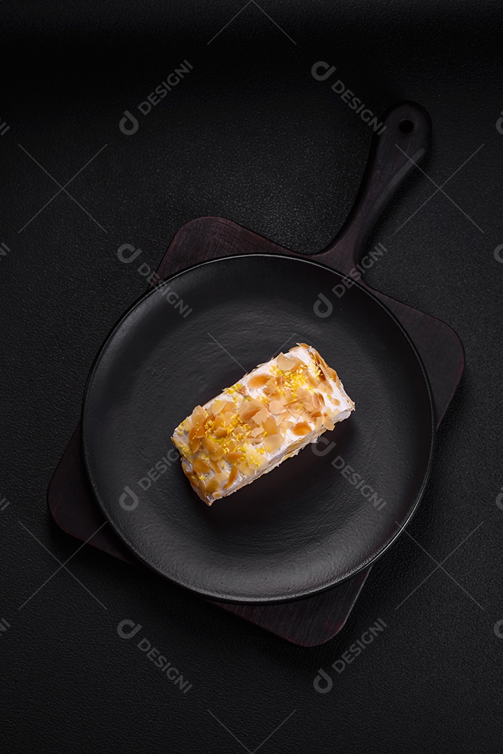Rolo de merengue delicioso, fresco e doce com creme, lascas de amêndoa, nozes e frutas cortadas em fatias sobre um fundo escuro de concreto
