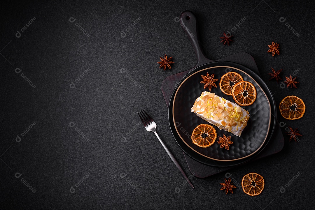 Rolo de merengue delicioso, fresco e doce com creme, lascas de amêndoa, nozes e frutas cortadas em fatias sobre um fundo escuro de concreto