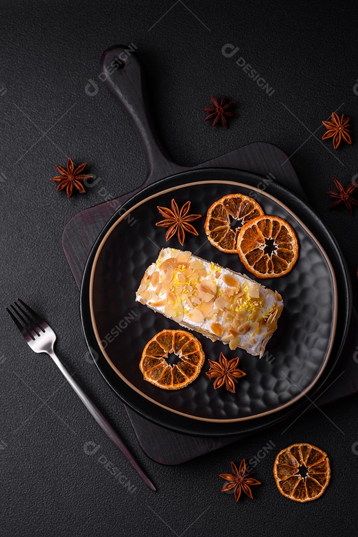 Rolo de merengue delicioso, fresco e doce com creme, lascas de amêndoa, nozes e frutas cortadas em fatias sobre um fundo escuro de concreto