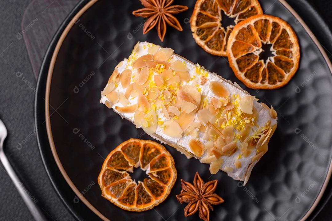 Rolo de merengue delicioso, fresco e doce com creme, lascas de amêndoa, nozes e frutas cortadas em fatias sobre um fundo escuro de concreto