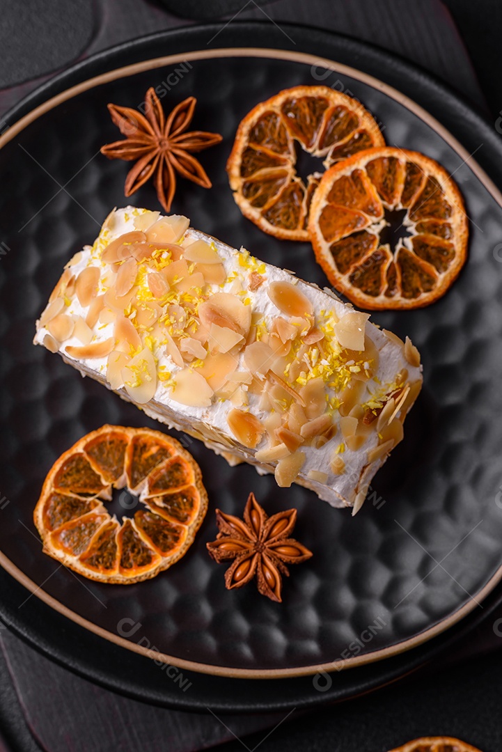 Rolo de merengue delicioso, fresco e doce com creme, lascas de amêndoa, nozes e frutas cortadas em fatias sobre um fundo escuro de concreto