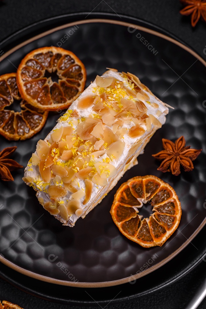 Rolo de merengue delicioso, fresco e doce com creme, lascas de amêndoa, nozes e frutas cortadas em fatias sobre um fundo escuro de concreto