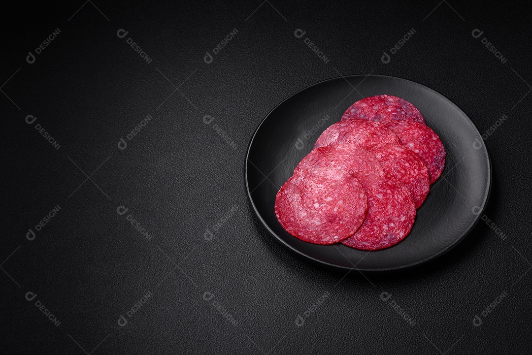 Deliciosa salsicha de salame fumado com sal, especiarias e ervas cortadas em fatias sobre um fundo escuro de concreto