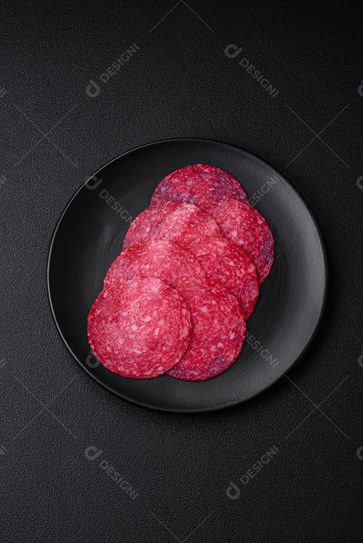 Deliciosa salsicha de salame fumado com sal, especiarias e ervas cortadas em fatias sobre um fundo escuro de concreto