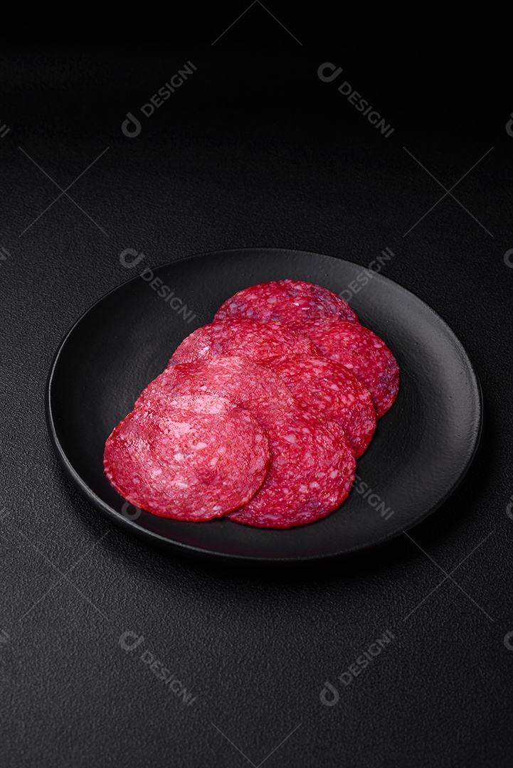 Deliciosa salsicha de salame fumado com sal, especiarias e ervas cortadas em fatias sobre um fundo escuro de concreto