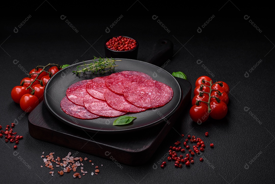 Deliciosa salsicha de salame fumado com sal, especiarias e ervas cortadas em fatias sobre um fundo escuro de concreto