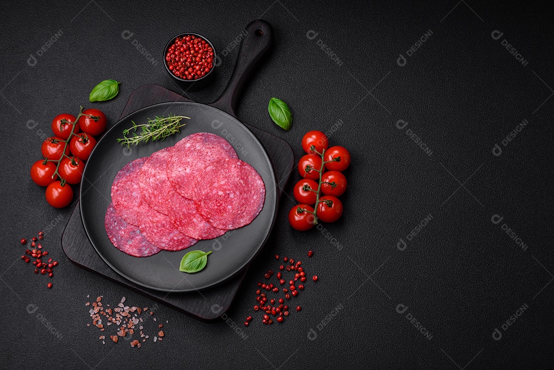 Deliciosa salsicha de salame fumado com sal, especiarias e ervas cortadas em fatias sobre um fundo escuro de concreto