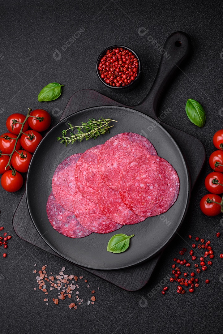 Deliciosa salsicha de salame fumado com sal, especiarias e ervas cortadas em fatias sobre um fundo escuro de concreto