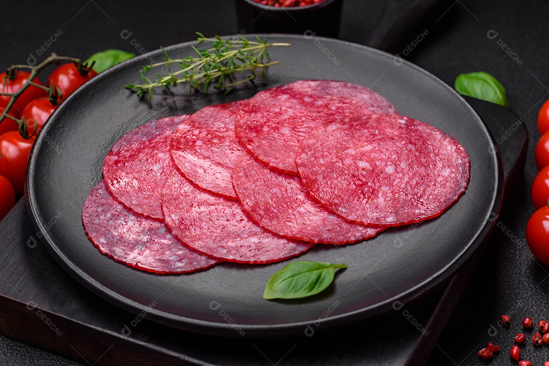 Deliciosa salsicha de salame fumado com sal, especiarias e ervas cortadas em fatias sobre um fundo escuro de concreto