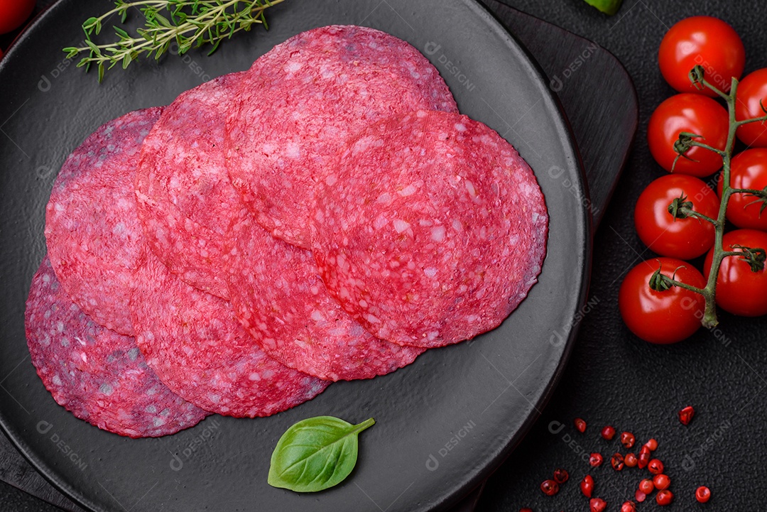 Deliciosa salsicha de salame fumado com sal, especiarias e ervas cortadas em fatias sobre um fundo escuro de concreto