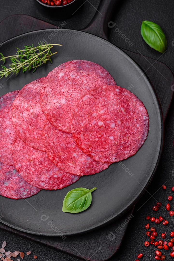 Deliciosa salsicha de salame fumado com sal, especiarias e ervas cortadas em fatias sobre um fundo escuro de concreto