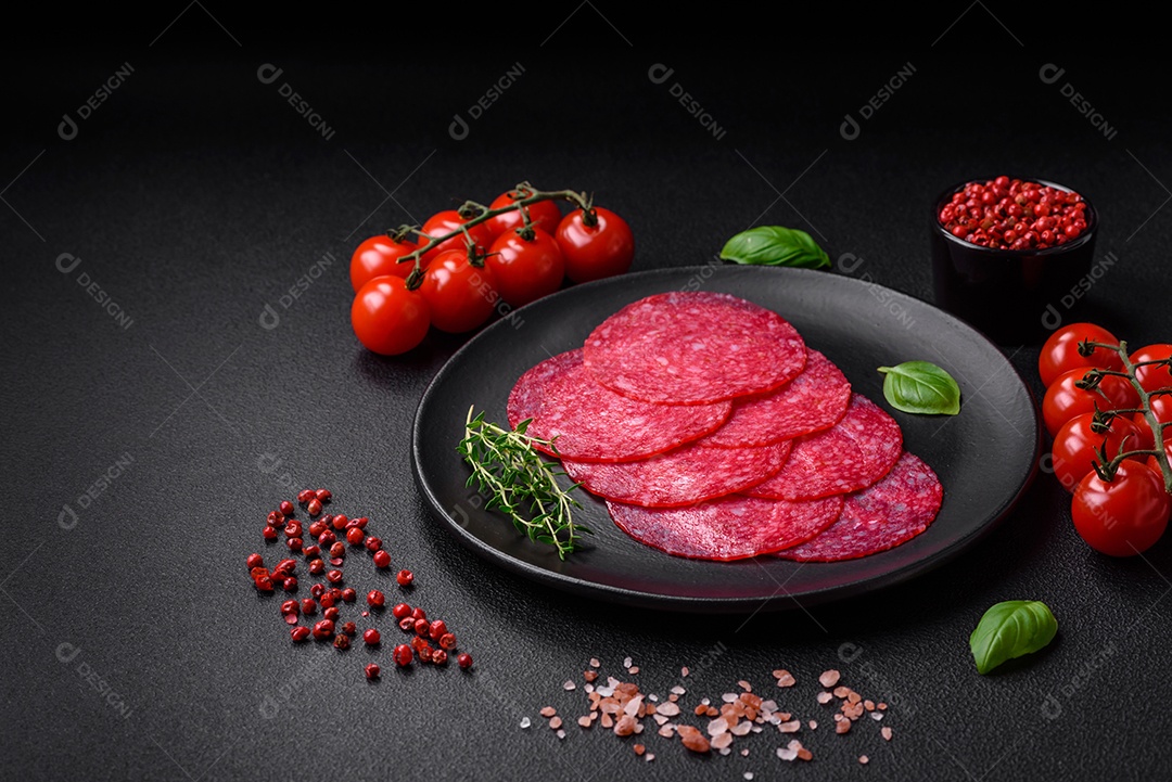 Deliciosa salsicha de salame fumado com sal, especiarias e ervas cortadas em fatias sobre um fundo escuro de concreto