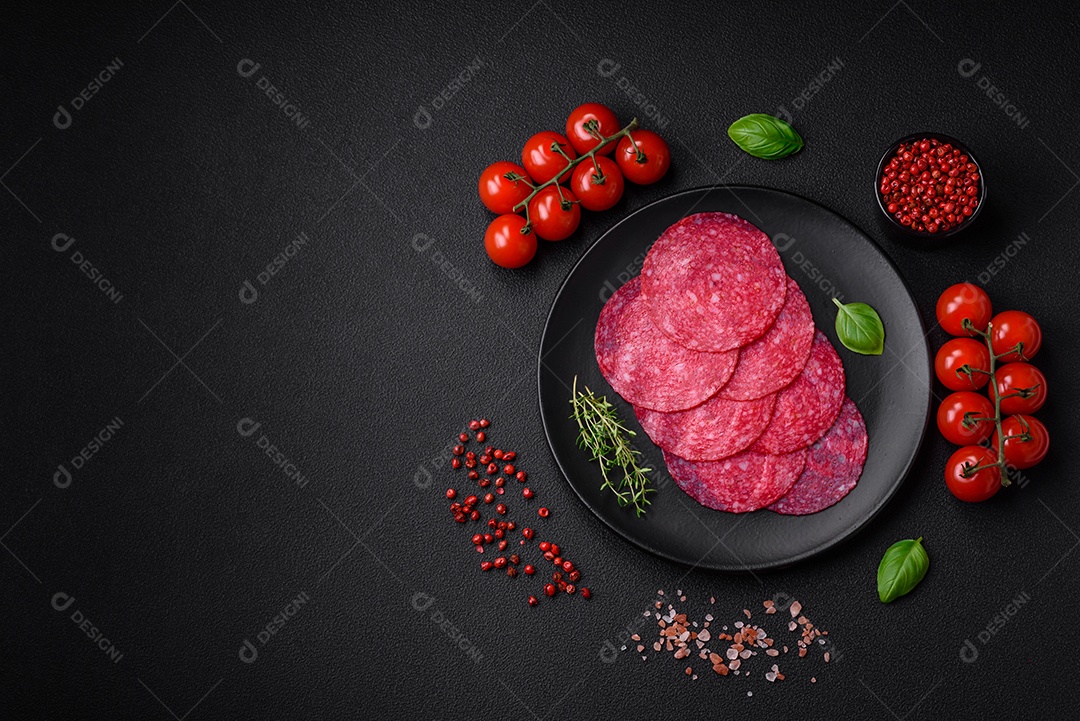 Deliciosa salsicha de salame fumado com sal, especiarias e ervas cortadas em fatias sobre um fundo escuro de concreto