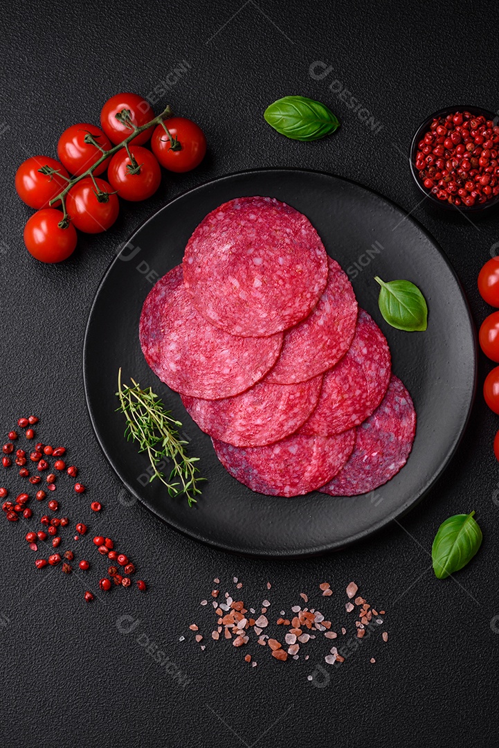 Deliciosa salsicha de salame fumado com sal, especiarias e ervas cortadas em fatias sobre um fundo escuro de concreto