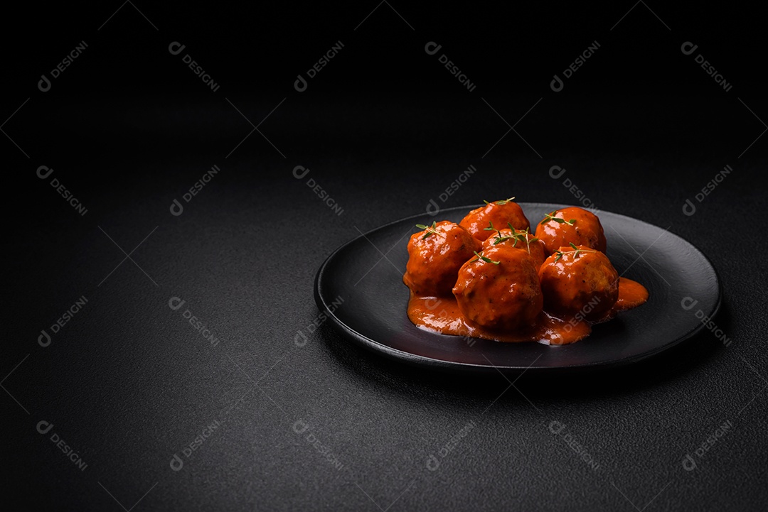 Deliciosas almôndegas frescas em molho de tomate com sal, especiarias e ervas sobre um fundo escuro de concreto