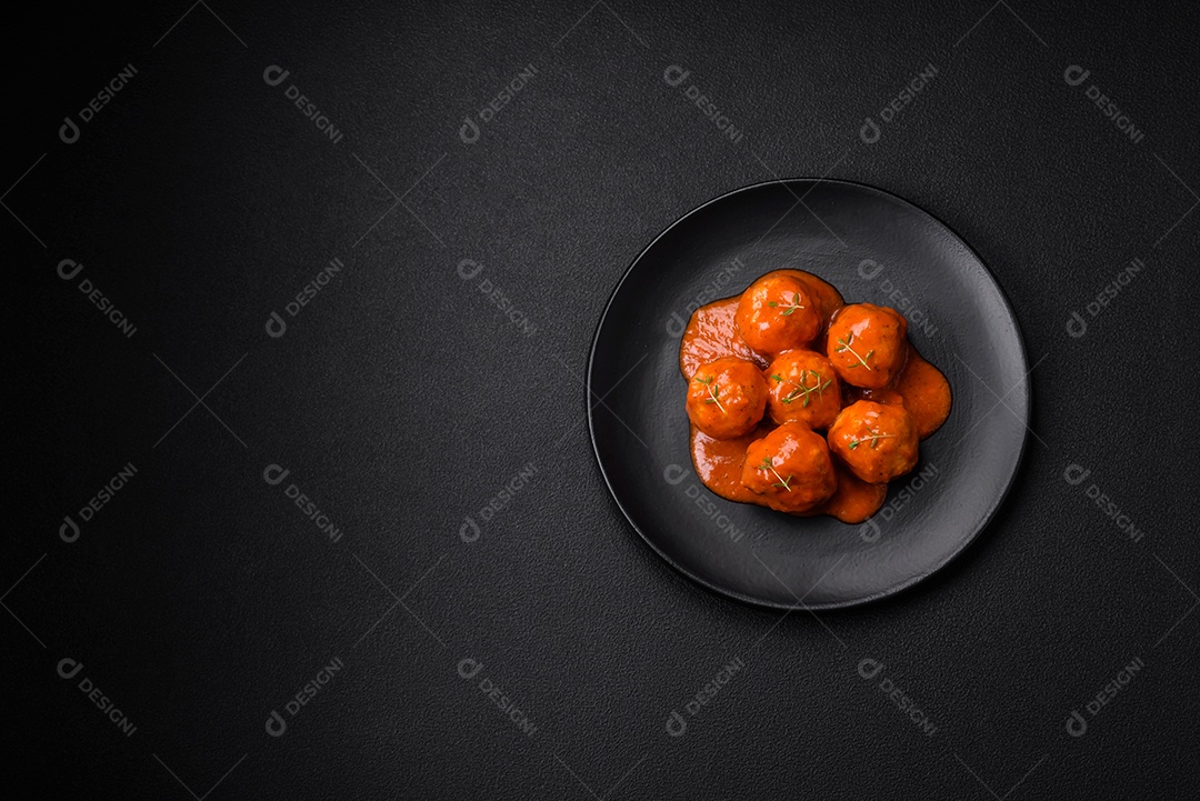 Deliciosas almôndegas frescas em molho de tomate com sal, especiarias e ervas sobre um fundo escuro de concreto
