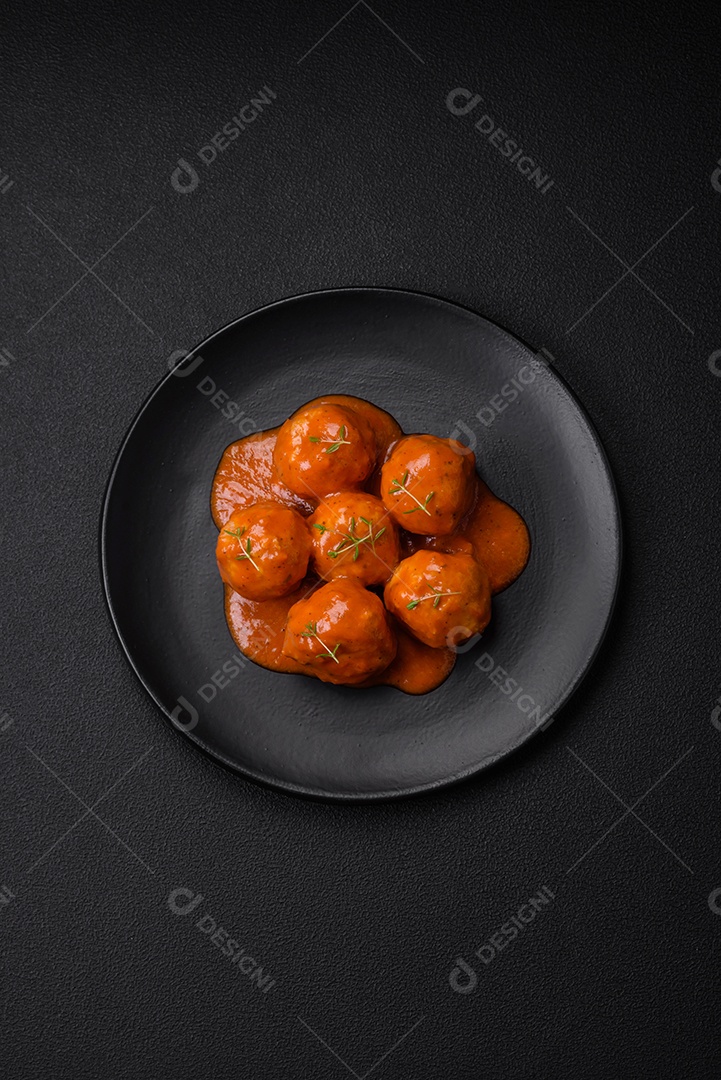 Deliciosas almôndegas frescas em molho de tomate com sal, especiarias e ervas sobre um fundo escuro de concreto