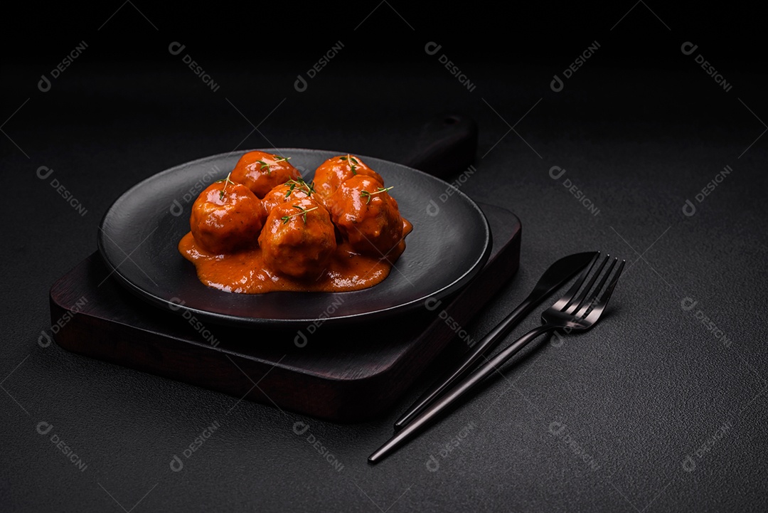 Deliciosas almôndegas frescas em molho de tomate com sal, especiarias e ervas sobre um fundo escuro de concreto