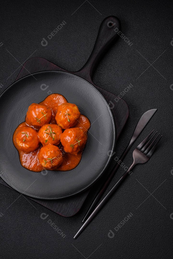 Deliciosas almôndegas frescas em molho de tomate com sal, especiarias e ervas sobre um fundo escuro de concreto