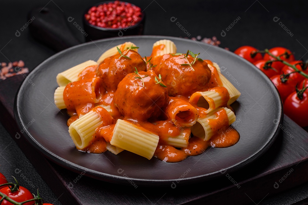 Deliciosas almôndegas frescas e massas em molho de tomate com sal, especiarias e ervas sobre um fundo escuro de concreto