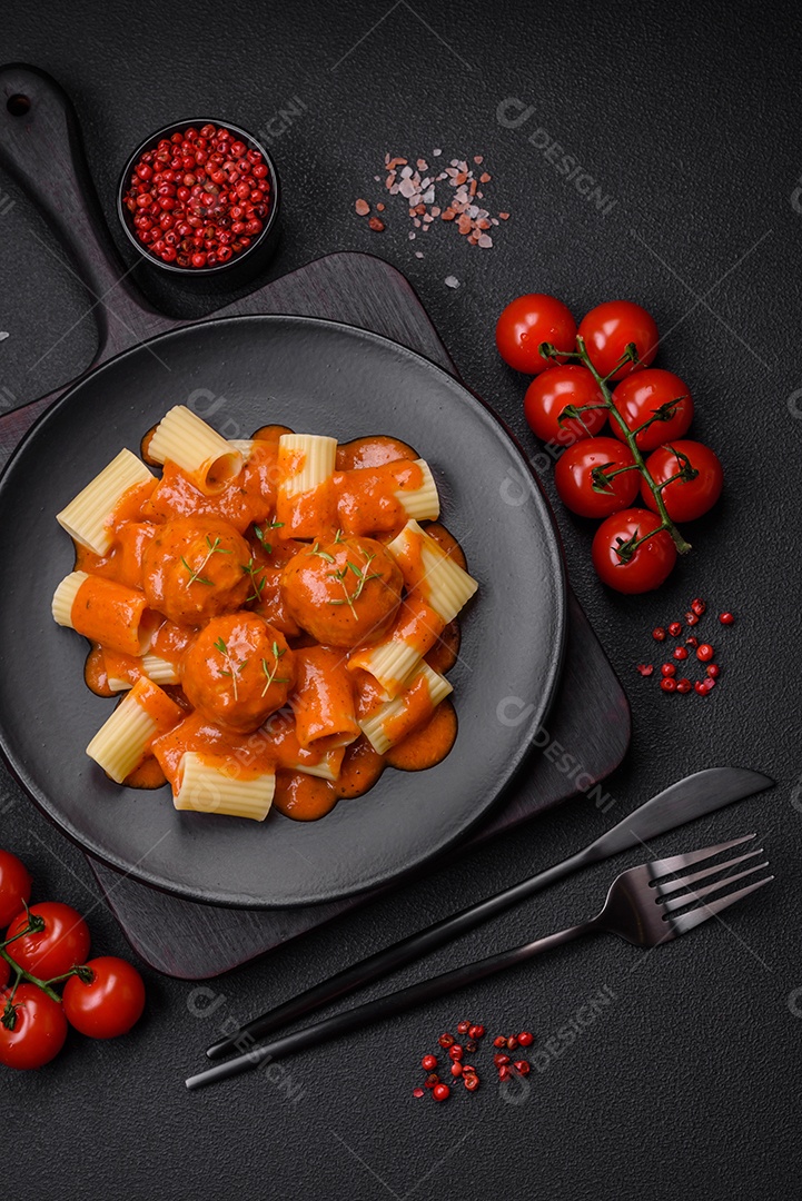 Deliciosas almôndegas frescas e massas em molho de tomate com sal, especiarias e ervas sobre um fundo escuro de concreto