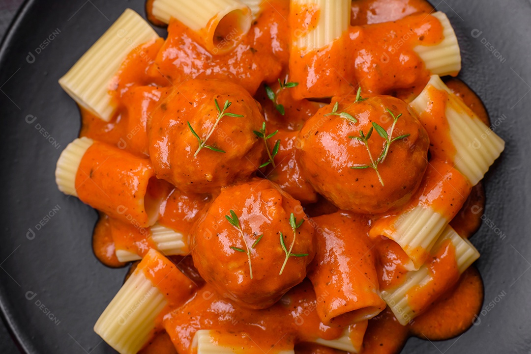 Deliciosas almôndegas frescas e massas em molho de tomate com sal, especiarias e ervas sobre um fundo escuro de concreto