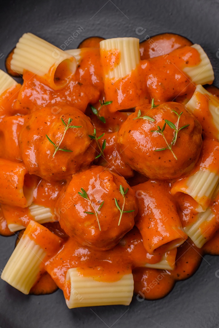 Deliciosas almôndegas frescas e massas em molho de tomate com sal, especiarias e ervas sobre um fundo escuro de concreto