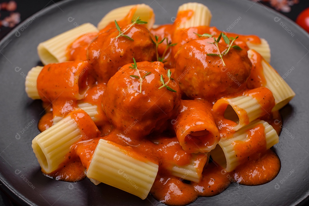 Deliciosas almôndegas frescas e massas em molho de tomate com sal, especiarias e ervas sobre um fundo escuro de concreto