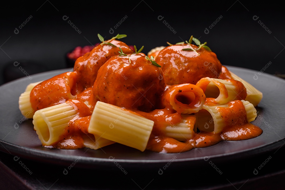 Deliciosas almôndegas frescas e massas em molho de tomate com sal, especiarias e ervas sobre um fundo escuro de concreto