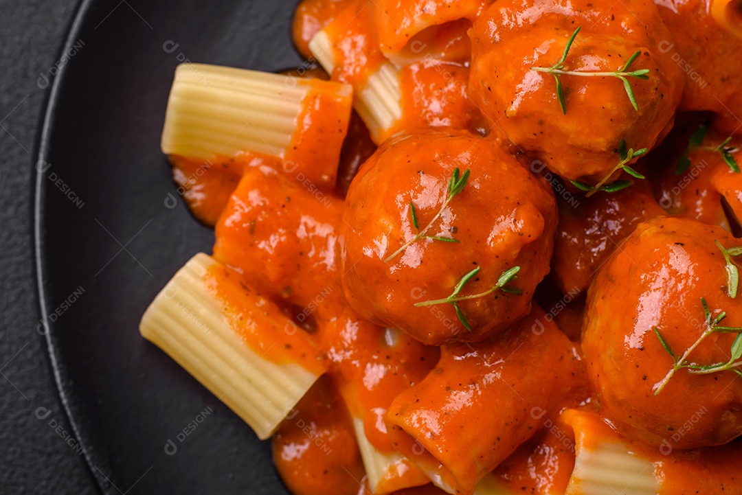 Deliciosas almôndegas frescas e massas em molho de tomate com sal, especiarias e ervas sobre um fundo escuro de concreto