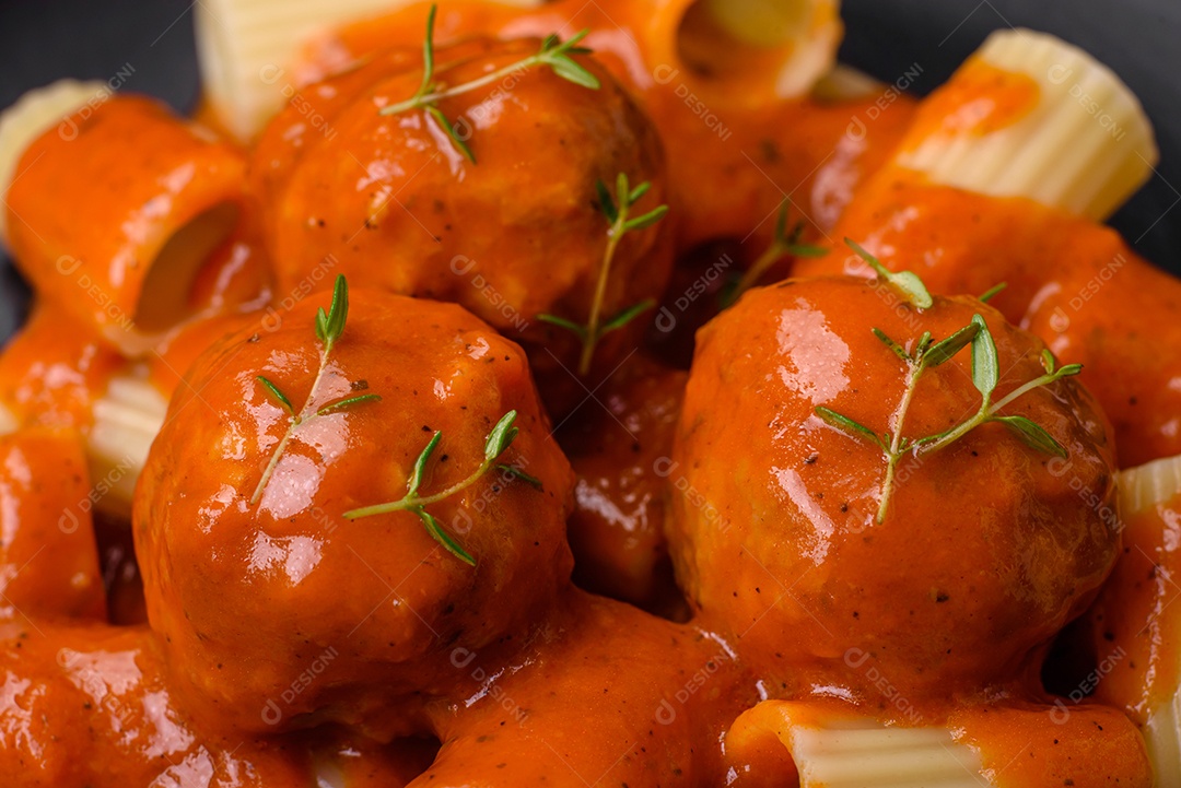 Deliciosas almôndegas frescas e massas em molho de tomate com sal, especiarias e ervas sobre um fundo escuro de concreto