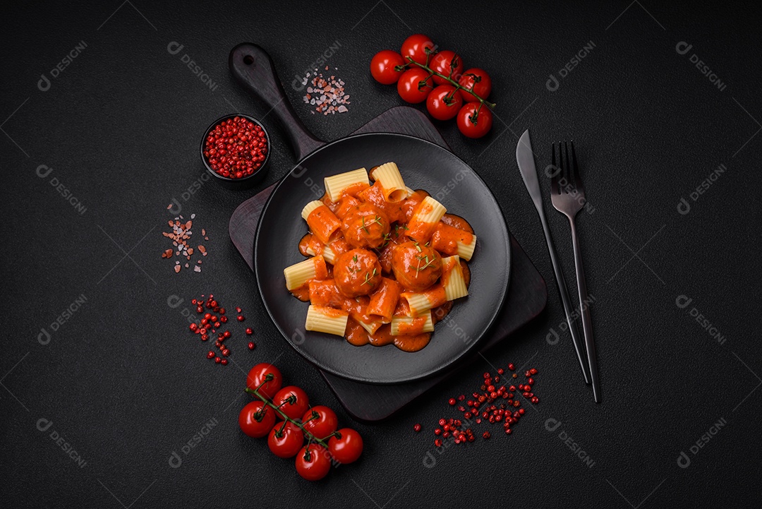Deliciosas almôndegas frescas e massas em molho de tomate com sal, especiarias e ervas sobre um fundo escuro de concreto