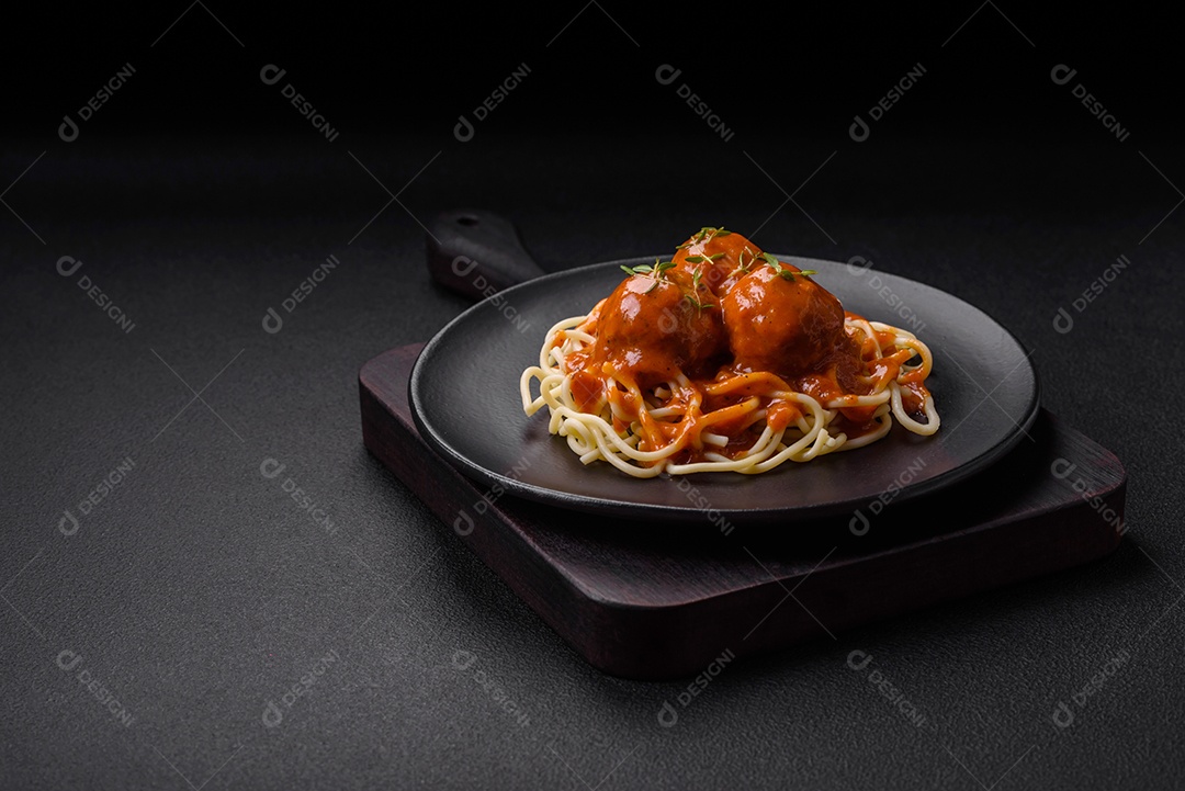 Deliciosas almôndegas frescas e massas em molho de tomate com sal, especiarias e ervas sobre um fundo escuro de concreto