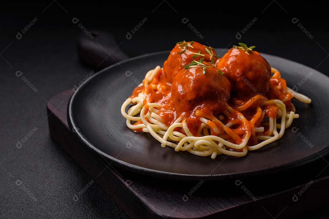 Deliciosas almôndegas frescas e massas em molho de tomate com sal, especiarias e ervas sobre um fundo escuro de concreto