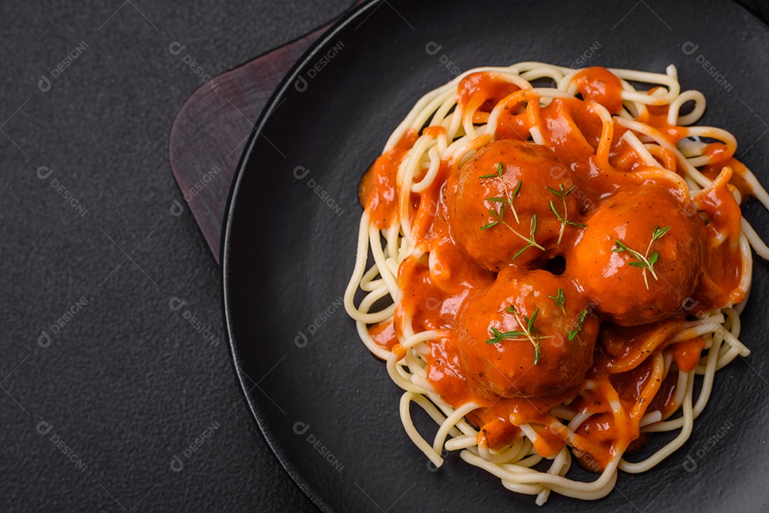 Deliciosas almôndegas frescas e massas em molho de tomate com sal, especiarias e ervas sobre um fundo escuro de concreto