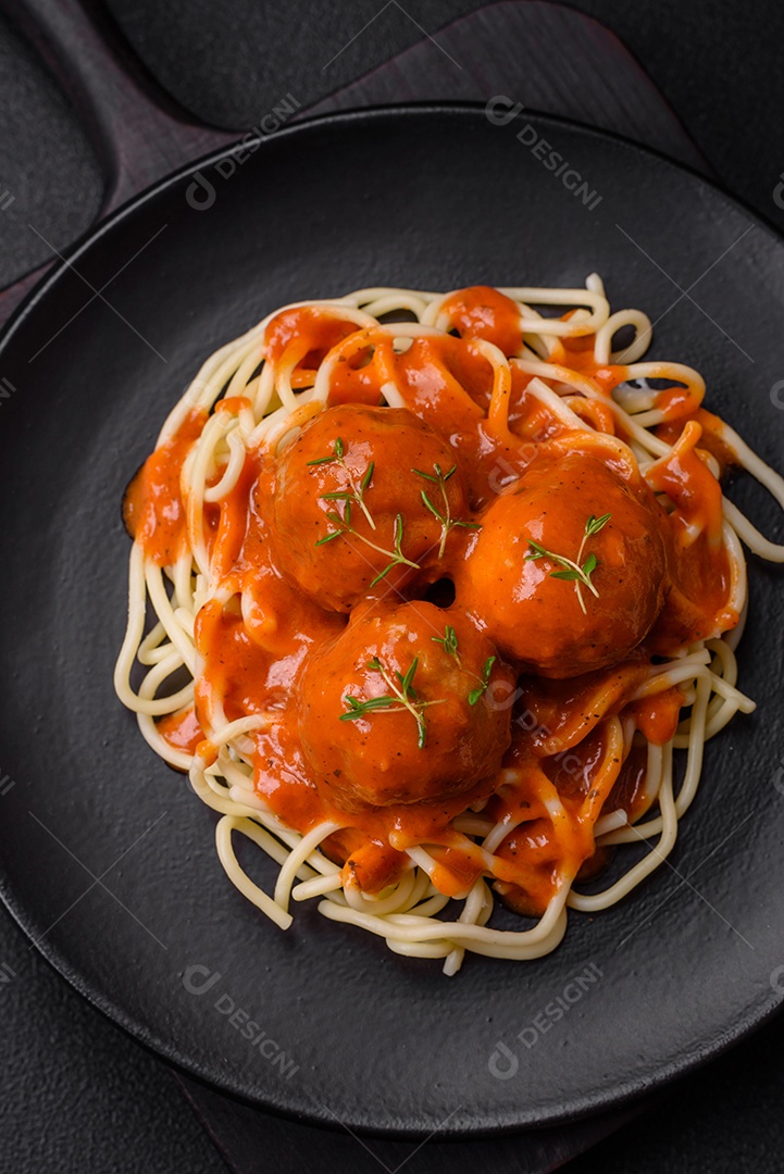 Deliciosas almôndegas frescas e massas em molho de tomate com sal, especiarias e ervas sobre um fundo escuro de concreto