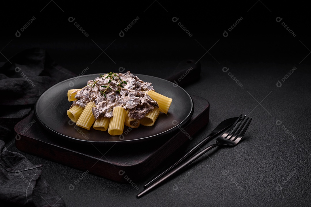 Deliciosa massa fresca com cogumelos champignon em molho cremoso com sal, especiarias e ervas sobre fundo escuro de concreto