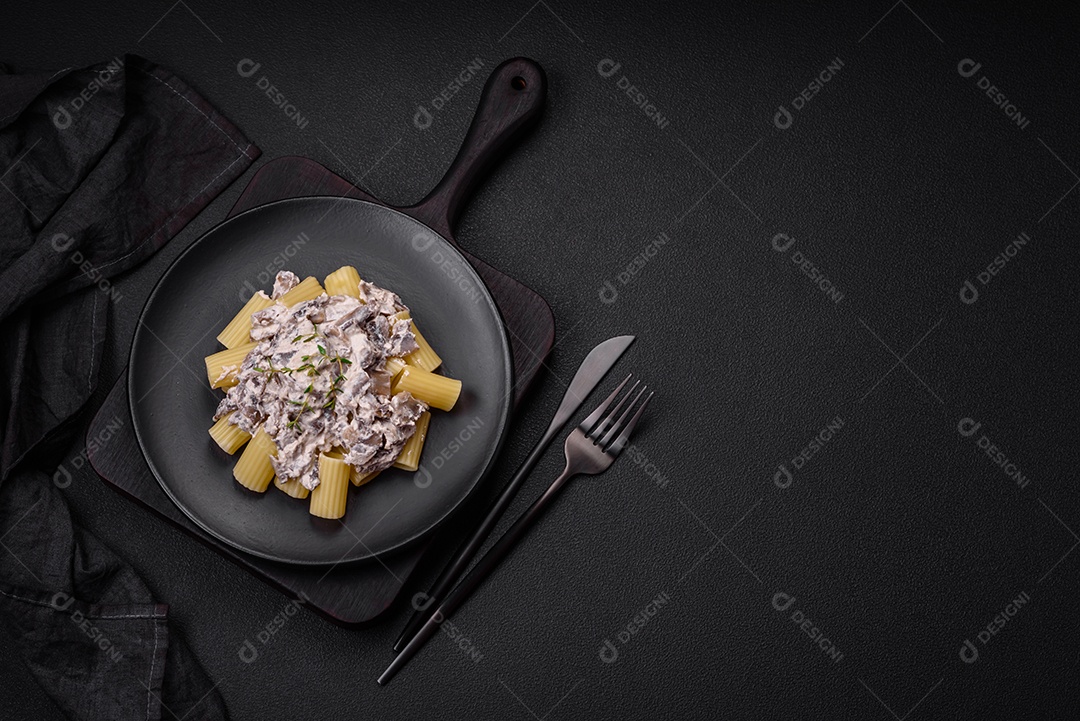 Deliciosa massa fresca com cogumelos champignon em molho cremoso com sal, especiarias e ervas sobre fundo escuro de concreto