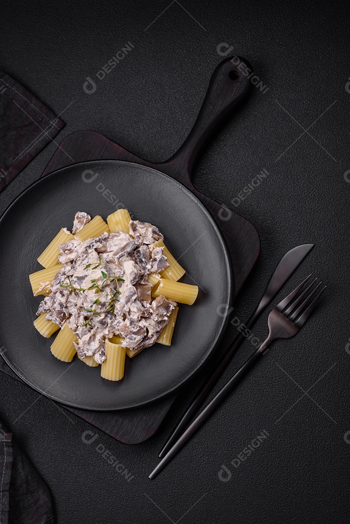 Deliciosa massa fresca com cogumelos champignon em molho cremoso com sal, especiarias e ervas sobre fundo escuro de concreto