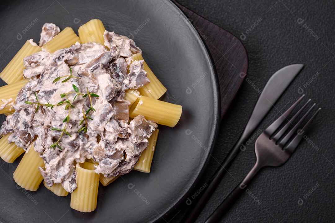 Deliciosa massa fresca com cogumelos champignon em molho cremoso com sal, especiarias e ervas sobre fundo escuro de concreto