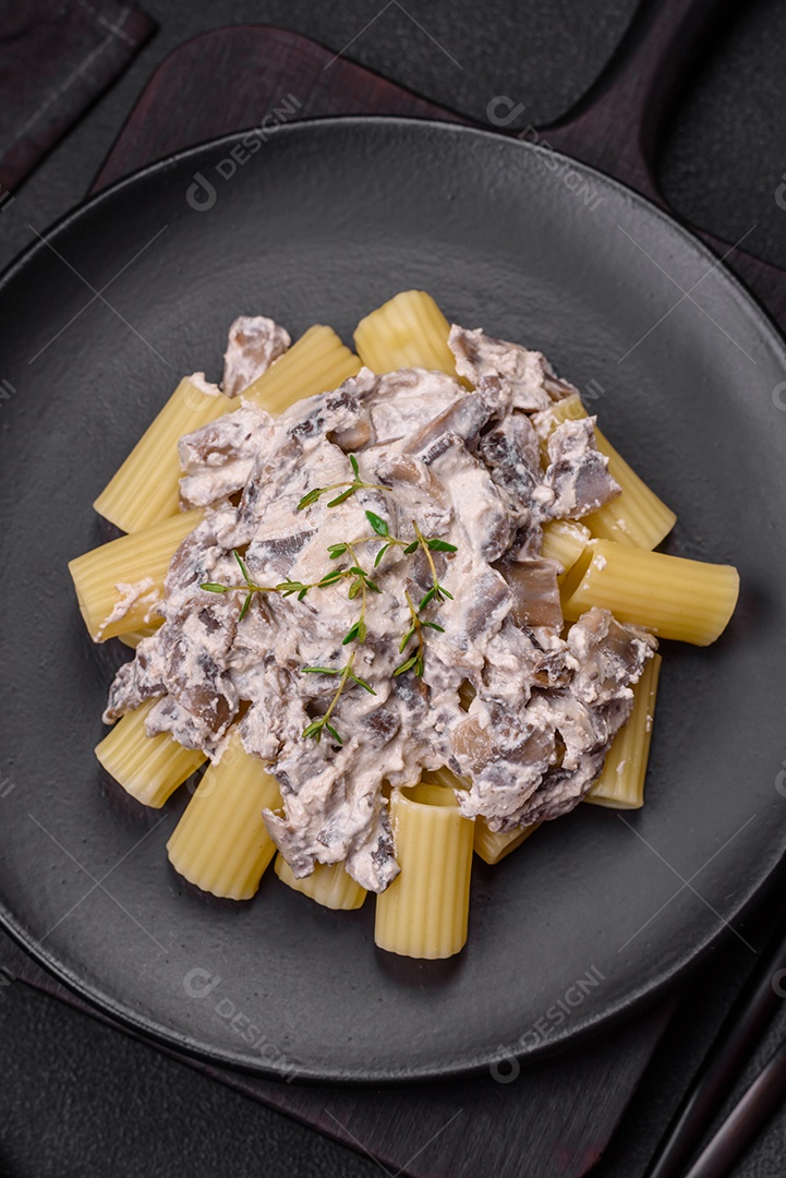 Deliciosa massa fresca com cogumelos champignon em molho cremoso com sal, especiarias e ervas sobre fundo escuro de concreto